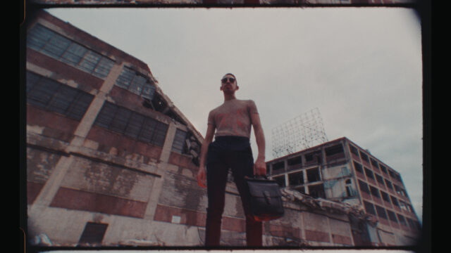 a film frame of a man standing in front of industrial buildings