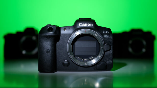 Canon EOS R5 camera before green background on a table, other cameras in background.