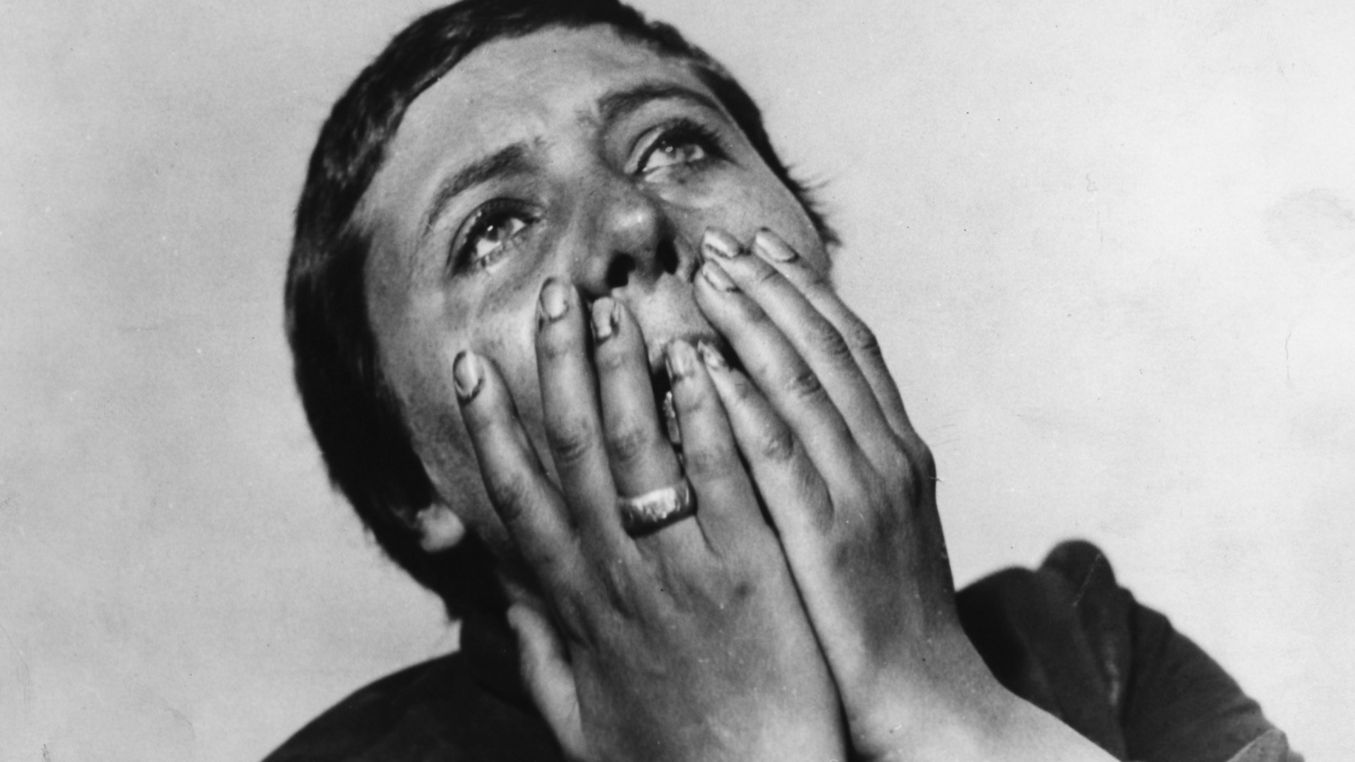 A close-up of the Joan's face struggling and covering it with her hands